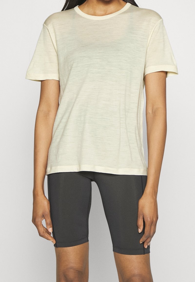 T-shirt a maniche corte di un beige chiaro con scollatura rotonda e texture morbida, abbinato a pantaloni corti neri aderenti. Design semplice e minimalista.