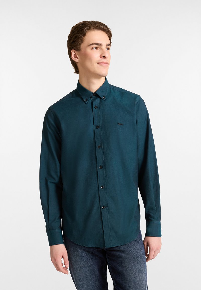 Donkerblauwe button-up shirt met lange mouwen en een puntige kraag, zwarte knopen, en een klein logo op de borst. Glad, lichtgewicht stof.