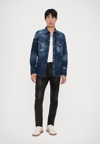 Denim overhemd in een donkere wassingen met vervaagde gebieden, twee voren zakken en zwarte mouwpatchdetails. Draag het met zwarte broeken en witte sneakers.