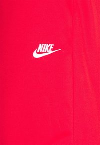 Tissu rouge Nike avec un logo blanc orné d'un design en forme de swoosh. Texture lisse, lignes épurées et couleur vibrante.
