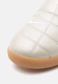 Δάχτυλο παπουτσιού από ελεφαντόδοντο δέρμα με ραφές σε σχήμα πλέγματος, λευκό λογότυπο Nike Swoosh κ αι ελαφρώς καφέ λαστιχένια σόλα.