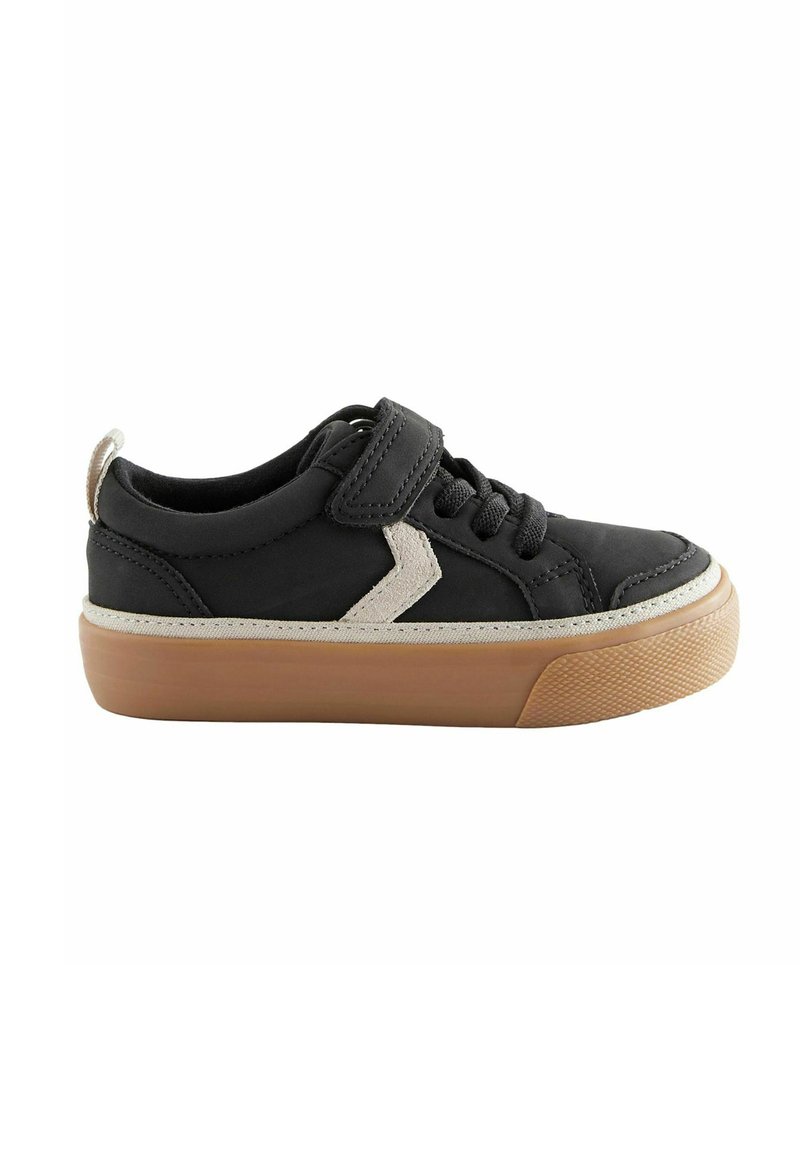 Black sneaker with a velcro strap, featuring a cream-colored accent and rubber sole. Rounded toe and textured surface details.