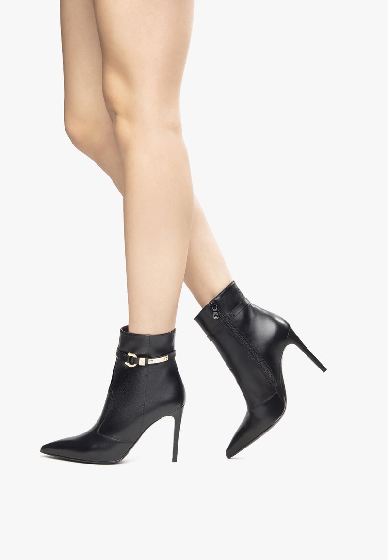 Black leather ankle boots with a pointed toe, high stiletto heel, buckle accent, and side zipper detail. Smooth texture throughout.