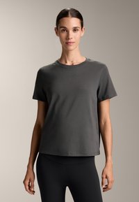 Siva bombažna majica s kratkimi rokavi, okroglo izrezana in ravnega kroja. Gladka tekstura, brez vzorcev, kombinirana z črnimi legicami.