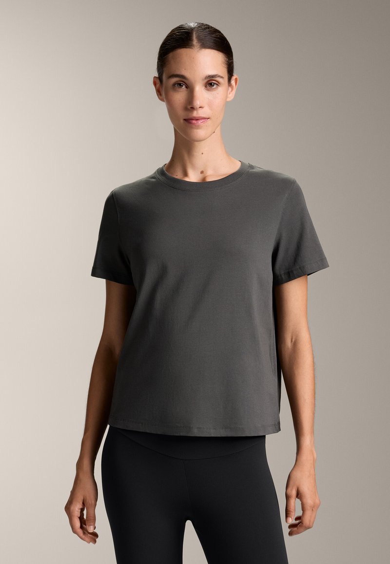 Siva bombažna majica s kratkimi rokavi, okroglo izrezana in ravnega kroja. Gladka tekstura, brez vzorcev, kombinirana z črnimi legicami.