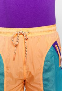 Oranžové šortky s šňůrkou, se smaragdově modrými síťovinovými bočními panely a fialovým akcentem. Lehký materiál, se strukturovaným povrchem.