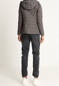 Grå dunjakke med vandret syning, en hætte, kombineret med mørke jeans og hvide sneakers. Den har en afslappet pasform og et enkelt design.