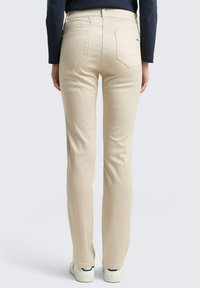 Beige, slim-fit broek met een lichte glans, voorzien van twee achterzakken en een duidelijk gedefinieerde tailleband, gecombineerd met witte sneakers.