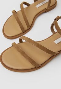 Sandalias de ante marrón con múltiples tiras delgadas y suela plana, con una plantilla beige suave y un diseño minimalista.
