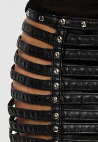 Zwarte leren rok met horizontale uitsparingen die de huid tonen en zilverkleurige metalen studs langs de voorste naad.