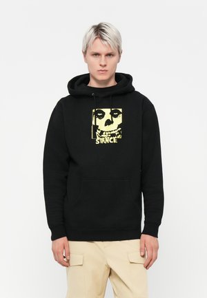 Black hoodie made of cotton with a front graphic featuring a skull and yellow text. Includes a kangaroo pocket and drawstring hood.