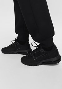 Melni Nike sporta apavi ar teksturētu sietu augšdaļu, auklīšu dizainu un melniem gumijas zoliņām. Iespējams redzēt gaisa spilvenu zolē.