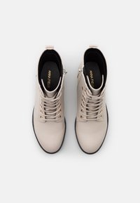 Stivali ankle beige in pelle liscia con punta rotonda, occhielli dorati e lacci; dotati di una zip laterale e suola nera.