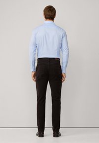 Lichtblauw overhemd met lange mouwen, gecombineerd met zwarte slim-fit broeken. Het shirt heeft een kraag en knopen bij de manchetten.