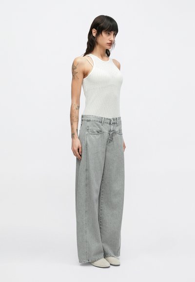 Débardeur blanc côtelé à fines bretelles, associé à un jean gris clair à coupe ample avec fermeture par boutons et légère décoloration.