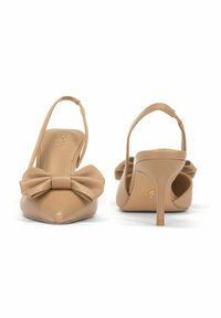 Beżowe skórzane sandały na obcasie z zaokrąglonym noskiem i dużą kokardą z przodu. Charakteryzują się smukłym, wysokim obcasem i otwartym tyłem.