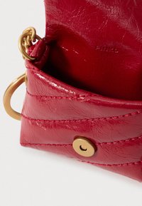 Saco de couro texturizado vermelho com ferragens douradas, apresentando um fecho de botão e um padrão decorativo cosido ao longo da superfície.