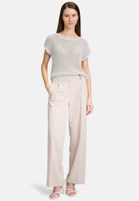 Lichtgrijs gebreid top met een losse pasvorm, gecombineerd met beige hoge taille wijde broek. Model draagt witte sandaaltjes met bandjes. Gladde textuur.