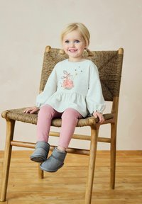 Gray sweatshirt with floral bunny design, pink leggings with stars, and gray ankle boots. Child sits on a wooden chair with woven seat.