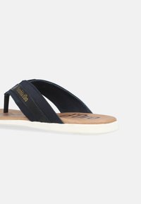 Marinblå flip-flops med textilremmar, en formad beige fotbädd och en vit gummisula. Har en logo på remmen och en strukturerad yta.