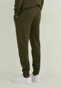 Olivgrüne Sweatpants mit entspannter Passform, gerippten Bündchen, Seitentaschen und glattem Material, kombiniert mit weißen Sneakers.