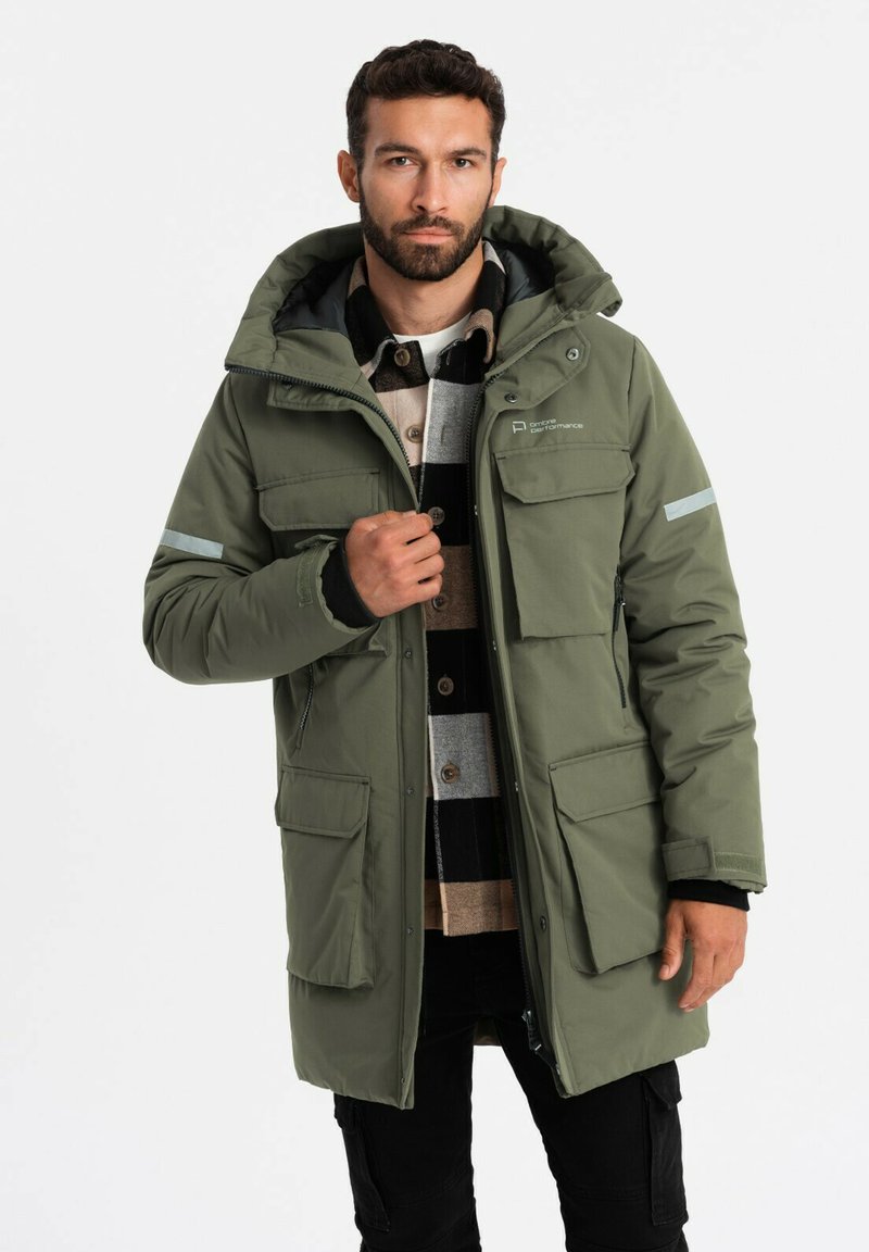 Parka isolante verde con cappuccio, dotata di molteplici tasche frontali e dettagli riflettenti. Il tessuto appare liscio e resistente.
