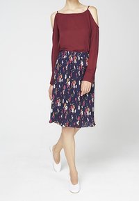 Blusa bordeaux off-shoulder abbinata a una gonna plissettata navy con fiori. La gonna presenta un mix di fiori vivaci su uno sfondo scuro. Ballerine bianche.