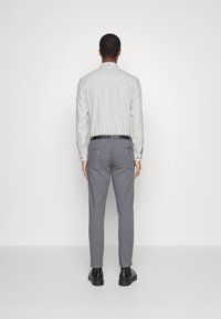 Camisa de manga larga gris claro con cuello abotonado, combinada con pantalones grises. Un cinturón negro y botas de tobillo completan el conjunto.