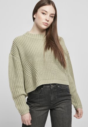 Pulover tricotat de culoare verde deschis, cu un design scurt, mâneci largi și guler ribat, asortat cu blugi negri. Detaliu de țesătură vizibil.