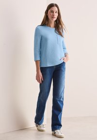 Lichtblauw, met textuur, langarm T-shirt met een zak, gecombineerd met recht gesneden, donkerblauwe jeans en witte sneakers. Eenvoudig en functioneel ontwerp.