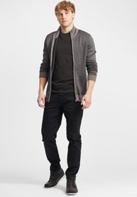 Cardigan gris con cremallera sobre una camiseta negra, combinado con jeans negros y botas de encaje gris oscuro. Texturas suaves, diseño ajustado.