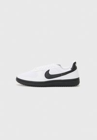 Hvide sportsko med en sort Nike swoosh, snøredesign, struktureret stofoverdel og sort gummisko.