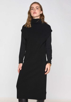 Black knitted dress with a high neck, long sleeves, and a loose fit. Features a textured fabric and knee-length design, with no prominent patterns.