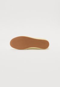 Soletta della scarpa con una forma liscia e arrotondata. Materiale superiore giallo, suola in gomma marrone e dettagli testurizzati vicino ai bordi.