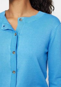 Ljusblå cardigan med rund halsringning, som har knäppning med knappar, ribbade ärmslut och en slät stickad textur.