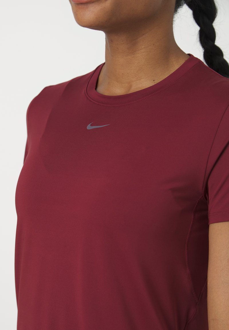 T-shirt de sport bordeaux à manches courtes, avec un col rond et un petit logo Nike gris sur la poitrine. Texture lisse et coupe ajustée.