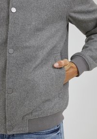 Grå ullblandingsjakke med trykknapper, sidelommer og ribbede mansjetter. Det teksturerte stoffet har en myk finish og et uformelt design.