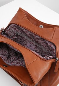 Bruine leren handtas met een voering van stof met bloemenpatroon. Het interieur bevat een vak met rits en een merklabel.