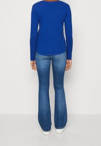 Sininen pitkähihaisen paita, jossa on pyöreä pääntie, yhdistettyinä leveälahkeisiin sinisiin farkkuihin ja valkoisiin lenkkareihin. Silkkinen kangasrunko, yksinkertainen muotoilu.