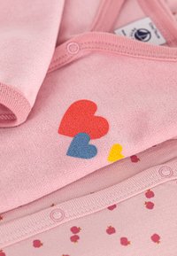 Tutina di tessuto rosa chiaro con motivo di cuori colorati in rosso, blu e giallo. Morbido al tatto con chiusure a pressione sul fondo.