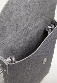 Sivá kožená crossbody taška s textúrovaným povrchom, jednoduchým dizajnom a magnetickým uzáverom. Interiér je vystlaný jemnou sivou textíliou.