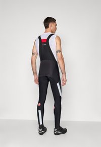 Shorts de cyclisme noirs avec un haut en maille, accents rouges, détails réfléchissants et design ajusté, comportant des zippers sur les jambes inférieures.