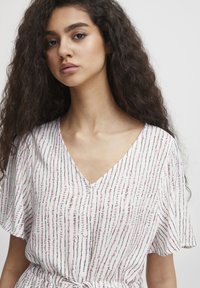 Hvid bluse med V-hals og korte, flagrende �ærmer. Har et lodret stribet mønster i pink og sort med dekorative knapper.