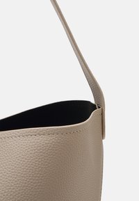 Sac à main en cuir beige avec une surface texturée et une bandoulière unique, présenté avec le dessus ouvert sur un fond uni.
