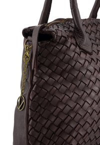 Brun læderhåndtaske med vævet tekstur, der har to håndtag, lynlåslukning og en dekorativ metalcharm. Glat finish, robust design.