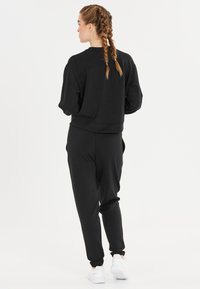 Zwarte fleece sweatshirt met lange mouwen en een ontspannen pasvorm, gecombineerd met bijpassende joggers. Bevat zijzakken en witte sneakers.