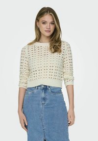 Gebreide trui in ivoorkleur met een drop stitch-patroon, ronde halslijn en lange mouwen, gecombineerd met een lichtblauwe denimrok met een voorkap.
