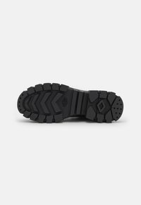 Semelle en caoutchouc noir avec des crampons profonds, des motifs en zigzag et des sections de grip circulaires. Durable et conçu pour une traction sur différentes surfaces.