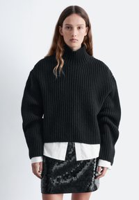 Black ribbed sweater with high neck and oversized sleeves, paired with a white button-up shirt and a black sequin skirt.