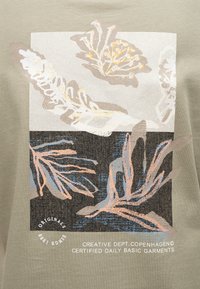 Formes botaniques abstraites en beige, brun, pêche et bleu sur un fond divisé clair et foncé avec le texte "Creative Dept. Copenhagen" sur tissu kaki.
